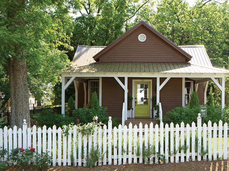 Brown cottage, green front door, and white picket fence. 
