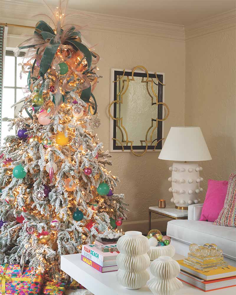 A flocked tree decorated with brightly colored ornaments and a tree topper made of sage ribbon and white featherrs.