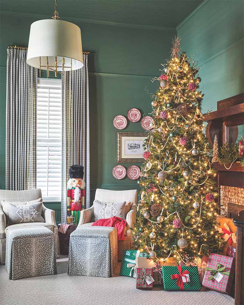 A hunter green study with a traditionally decorated tree and a pair of grey arm chairs. 