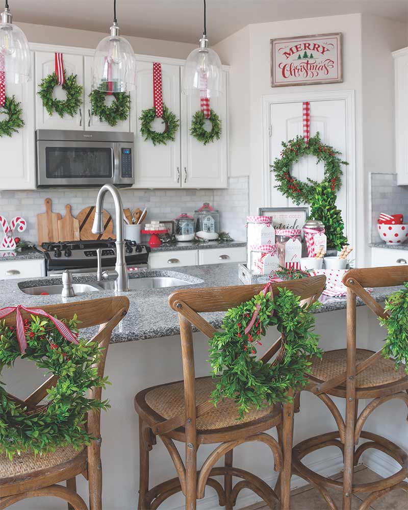 A kitchen decorated with a medley of miniature green wreaths hung on chairs and cabinets with red ribbon