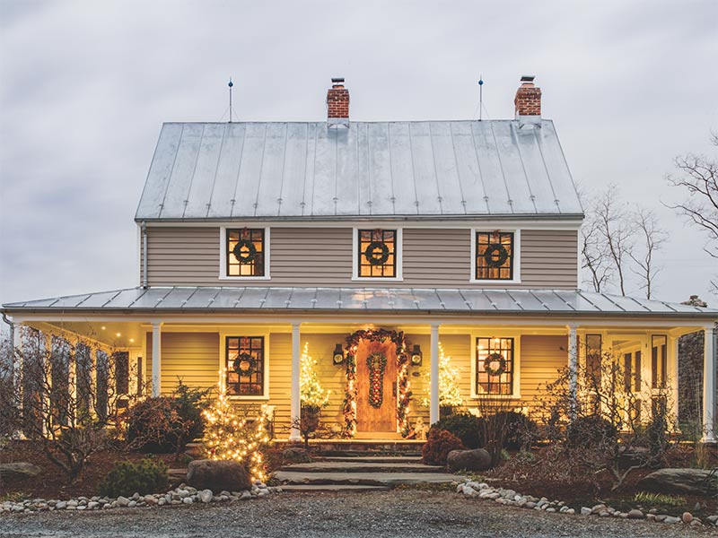 The exterior of a farmhouse decorated with lights and greenery. 