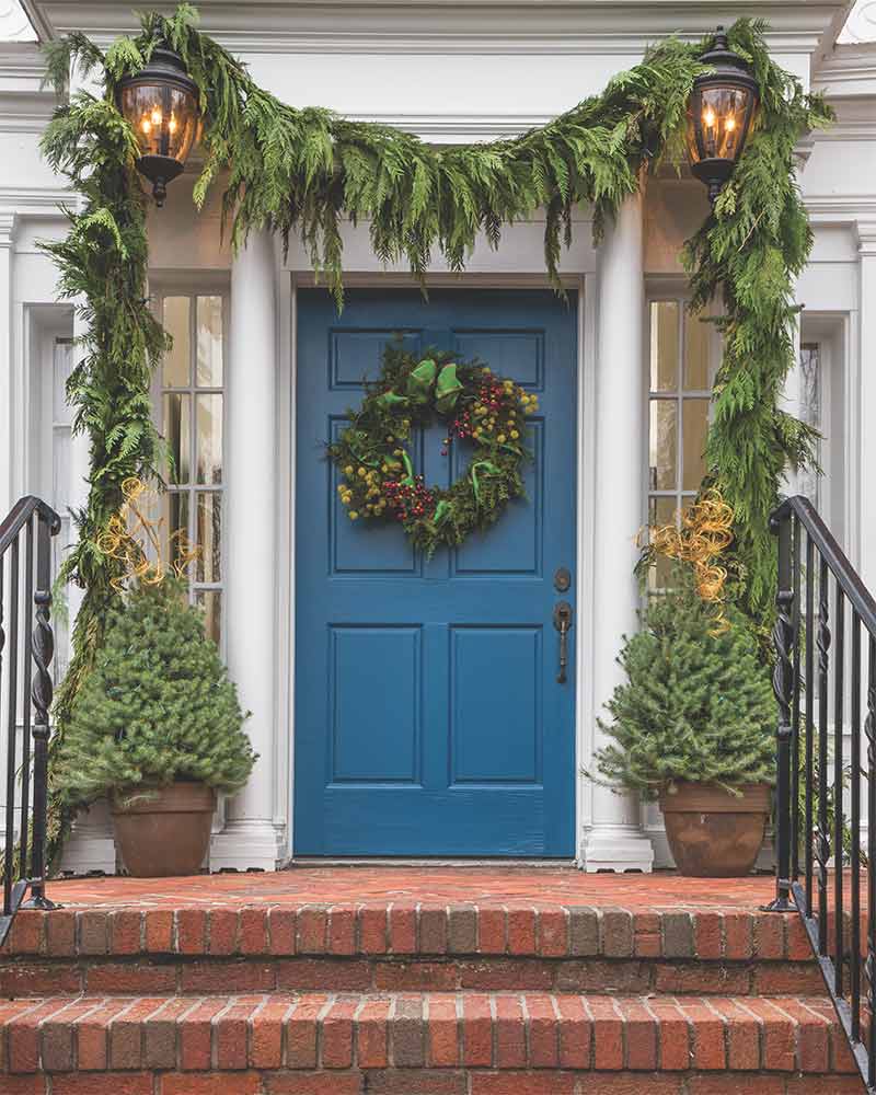 A front door decorated with a garland of fresh greenery and a holiday wreath. 