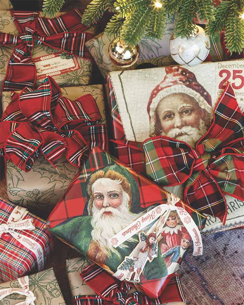 A pile of presents with paper cutouts of Santa glued to plaid wrapping paper. 