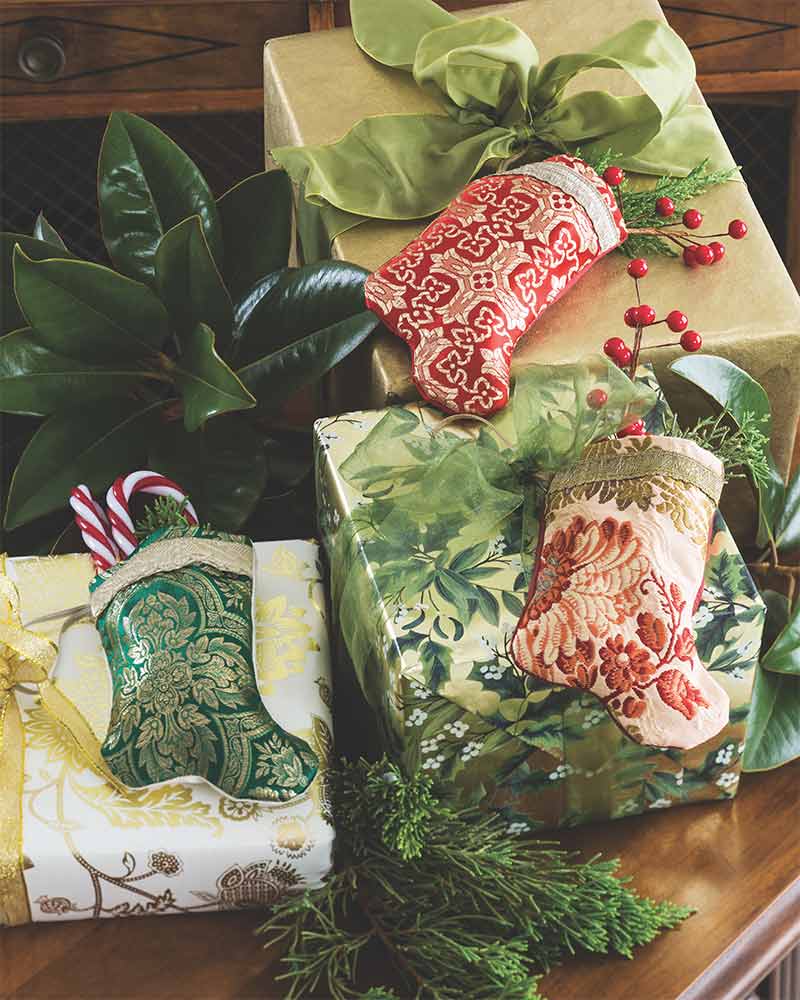 Miniature embroidered stockings stuffed with greenery and affixed with ribbon to packages.