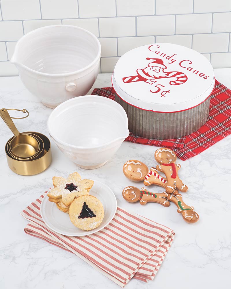 White mixing bowls, gold measuring cups, gingerbread measuring spoons, and a galvanized storage container. 