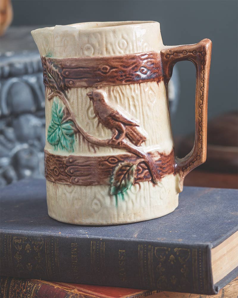 A Majolica pitcher with a bird and tree branch design. 
