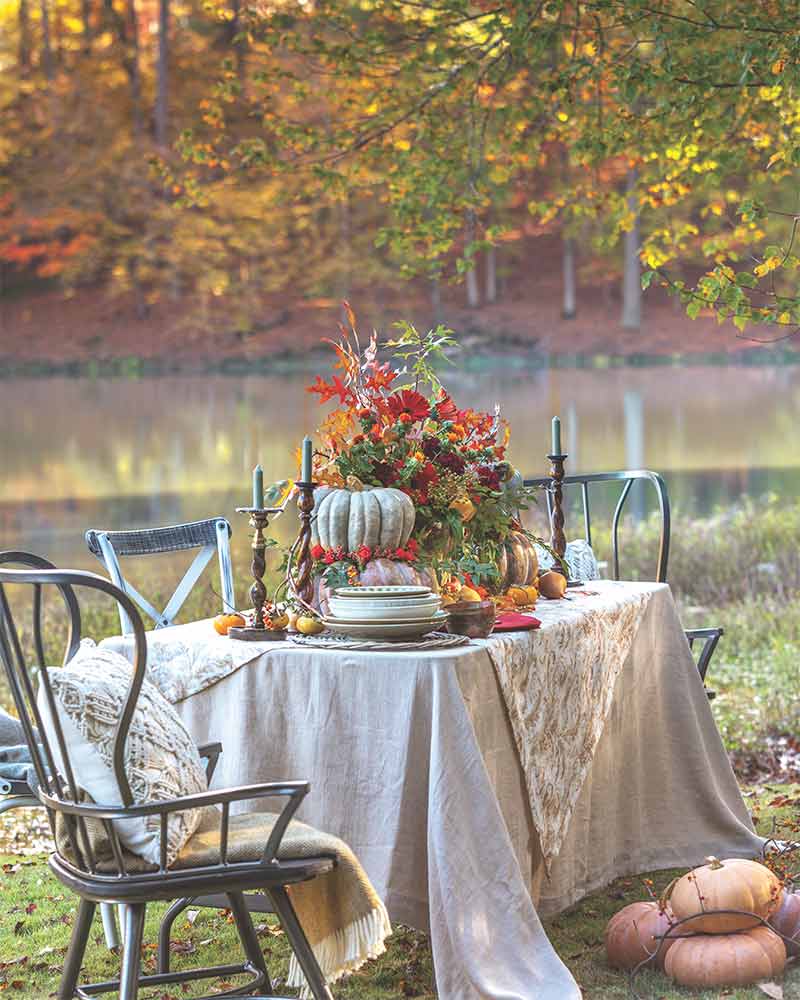 A lakeside alfresco tablescape with neutral linens and colorful fall foliage. 