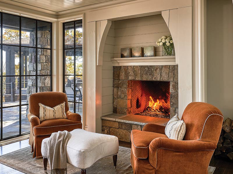A pair of brown armchairs and a white ottoman in front of a fire. 