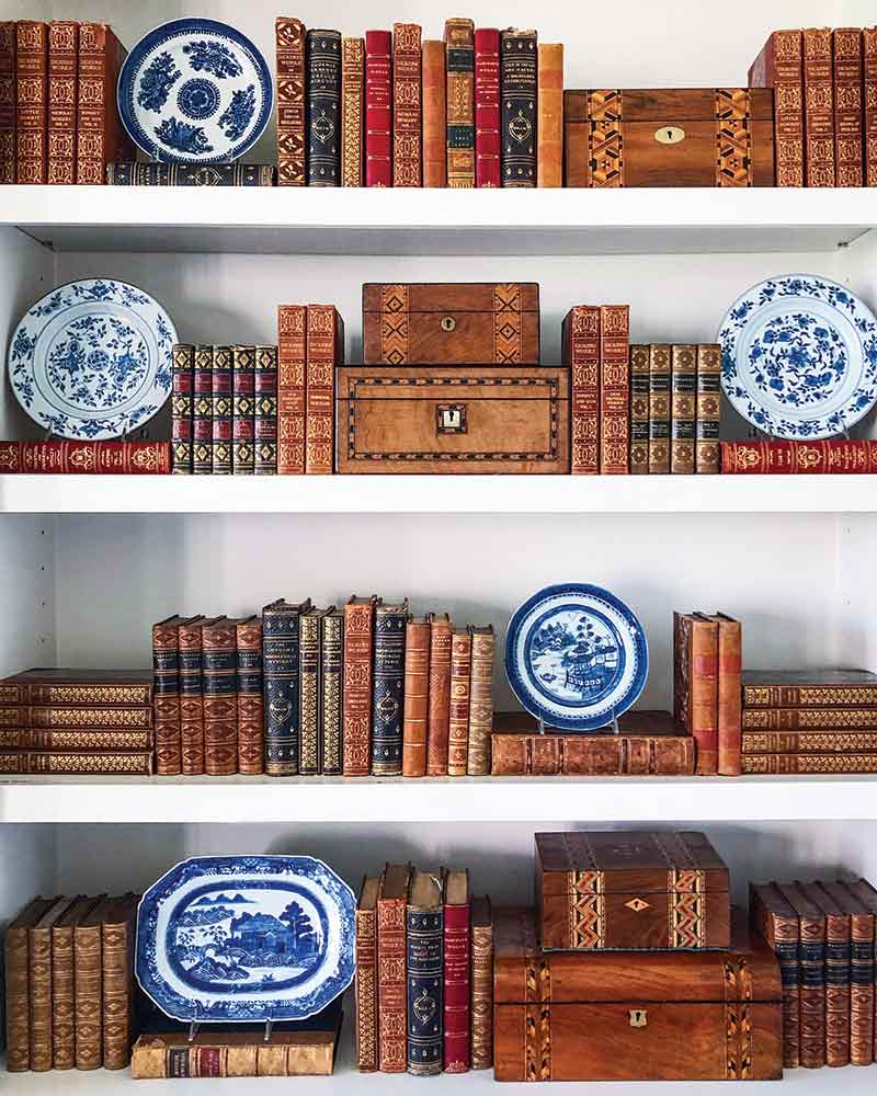 A bookshelf decorated with antique books, boxes, and blue-and-white china.