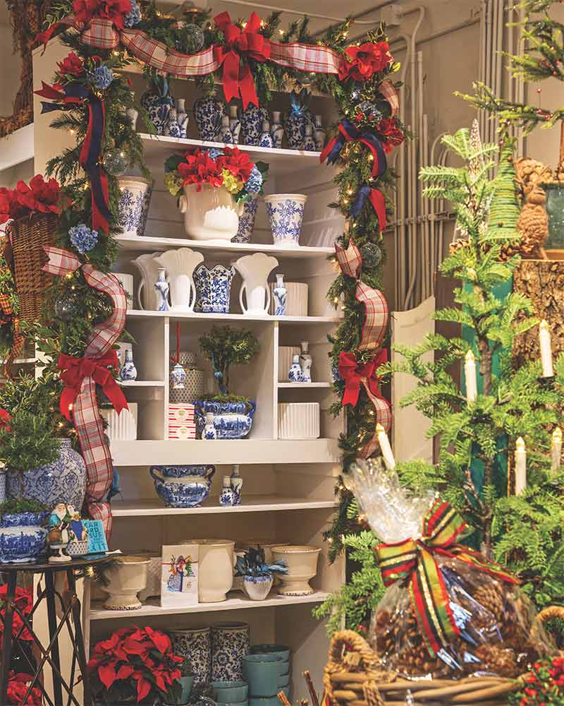 A garland with red ribbon draped around a shelf of blue-and-white vases. 