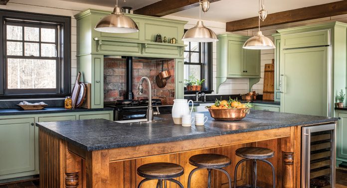 A kitchen painted sage with a wood island and black countertops