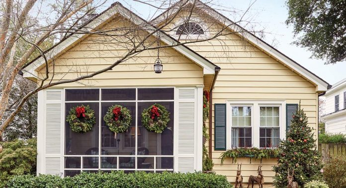 The front exterior of a yellow home featuring a trio of wreaths with red bows.
