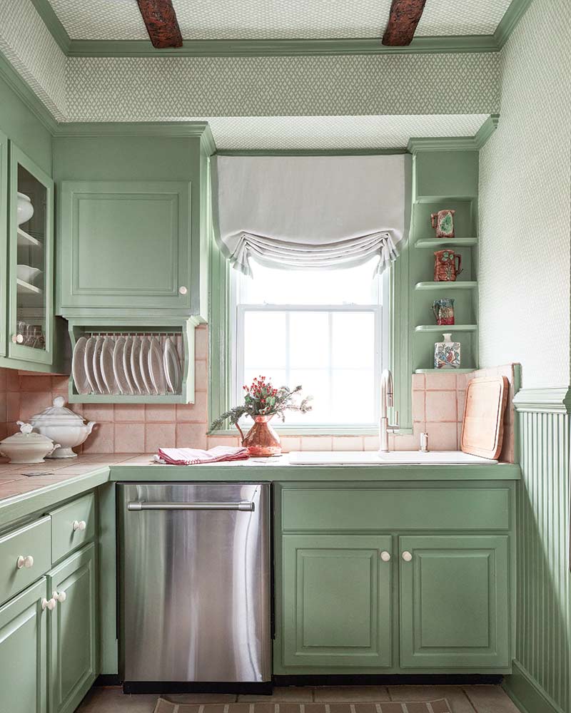 A kitchen painted pistachio green with a wallpapered ceiling. 