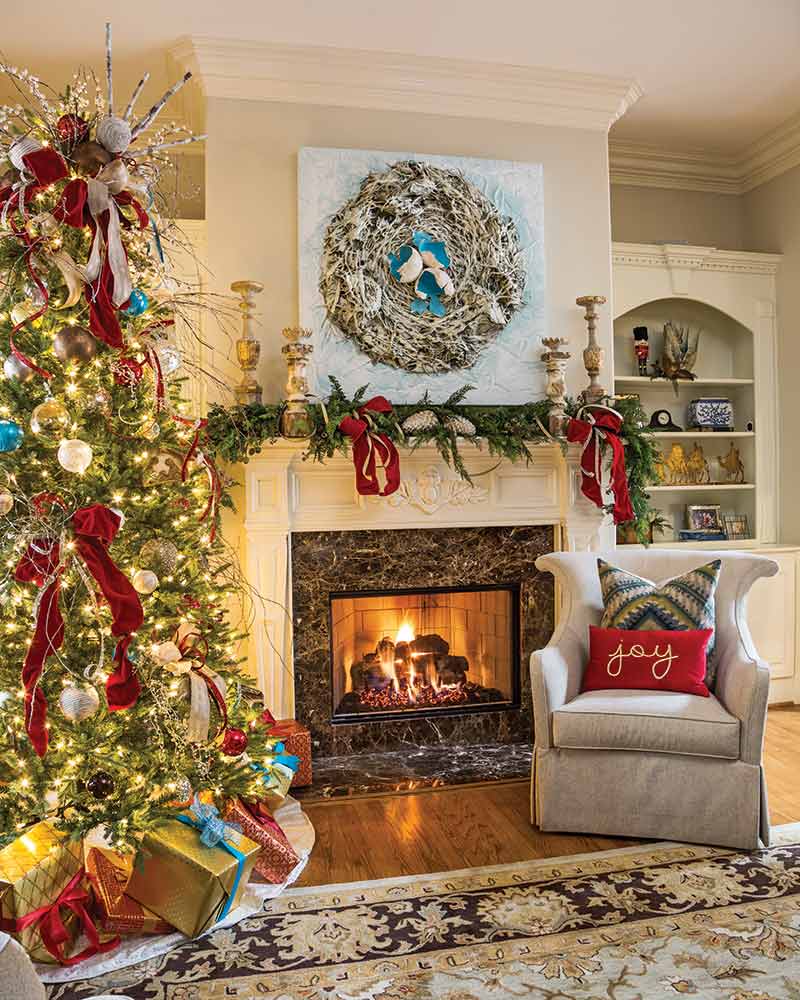 A Christmas tree in a living room with an abstract painting above the mantel. 