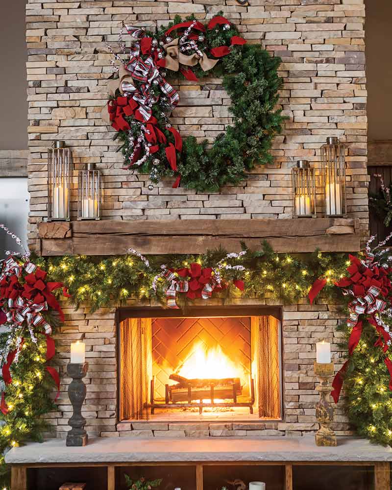A stone fireplace with a large wreath and garland decorated with ribbon.