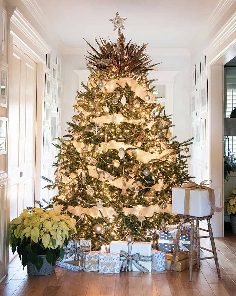 An expansive tree decorated with white ornaments and and surrounded by neutral packages and an ivory poinsettia. 