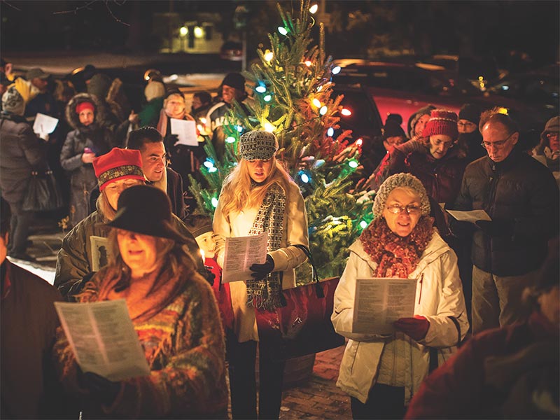 A group gathered around a Christmas tree singing carols.