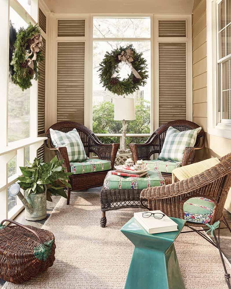 A sun room with wicker furnishings and green cushions.