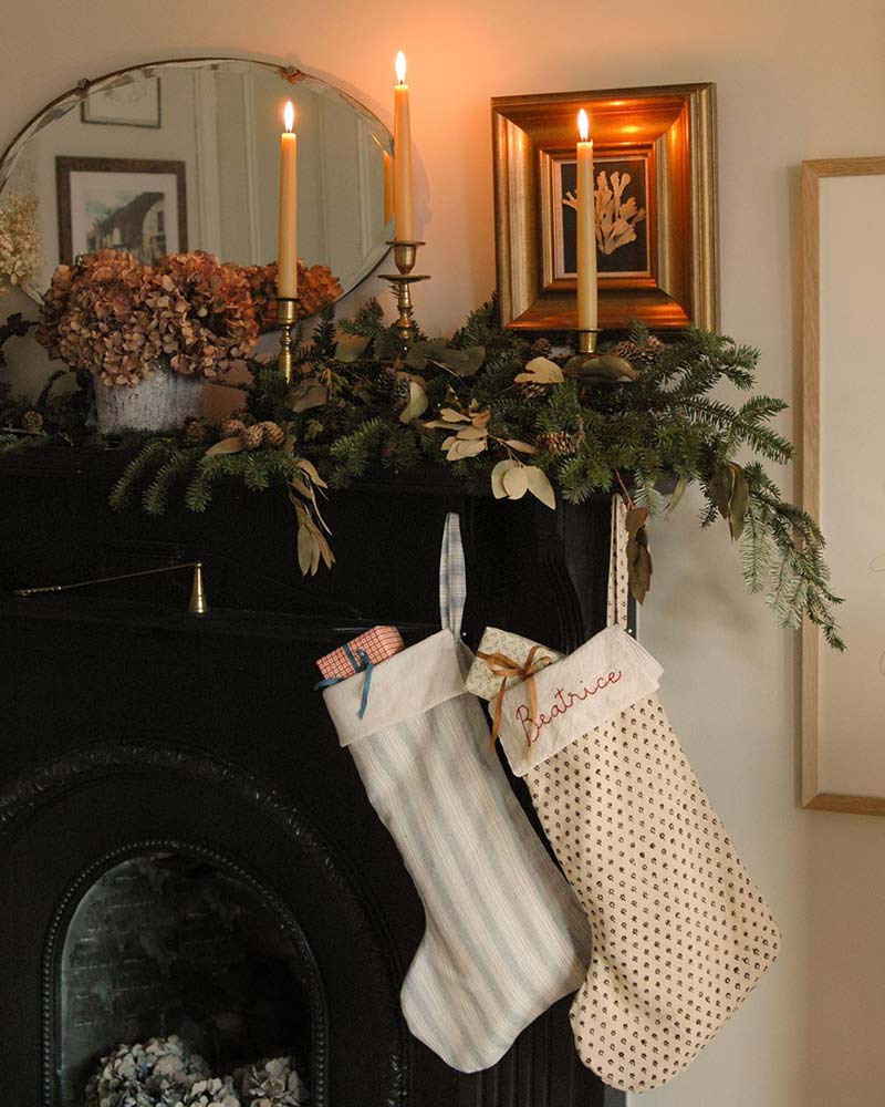 A mantel decorated with hand-stitched stockings, dried hydrangeas, and taper candles.