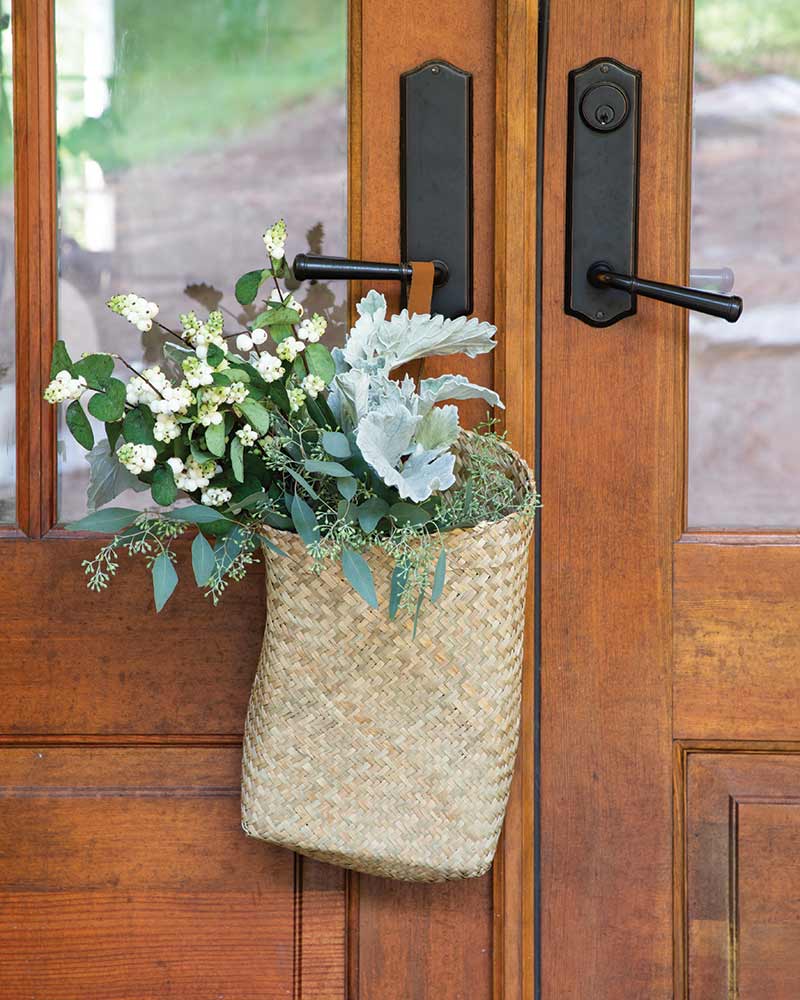 A woven basket with fresh greenery hanging from a front door.
