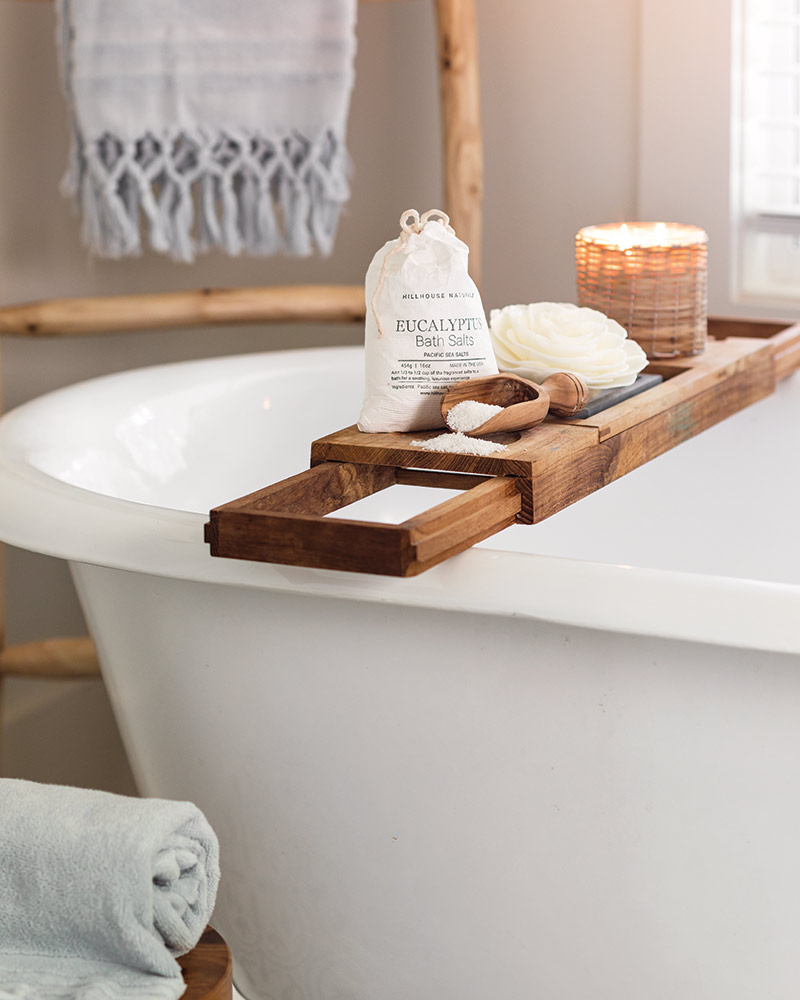 A bathtub with a shelf displaying bath salts, floral soap, and a candle.