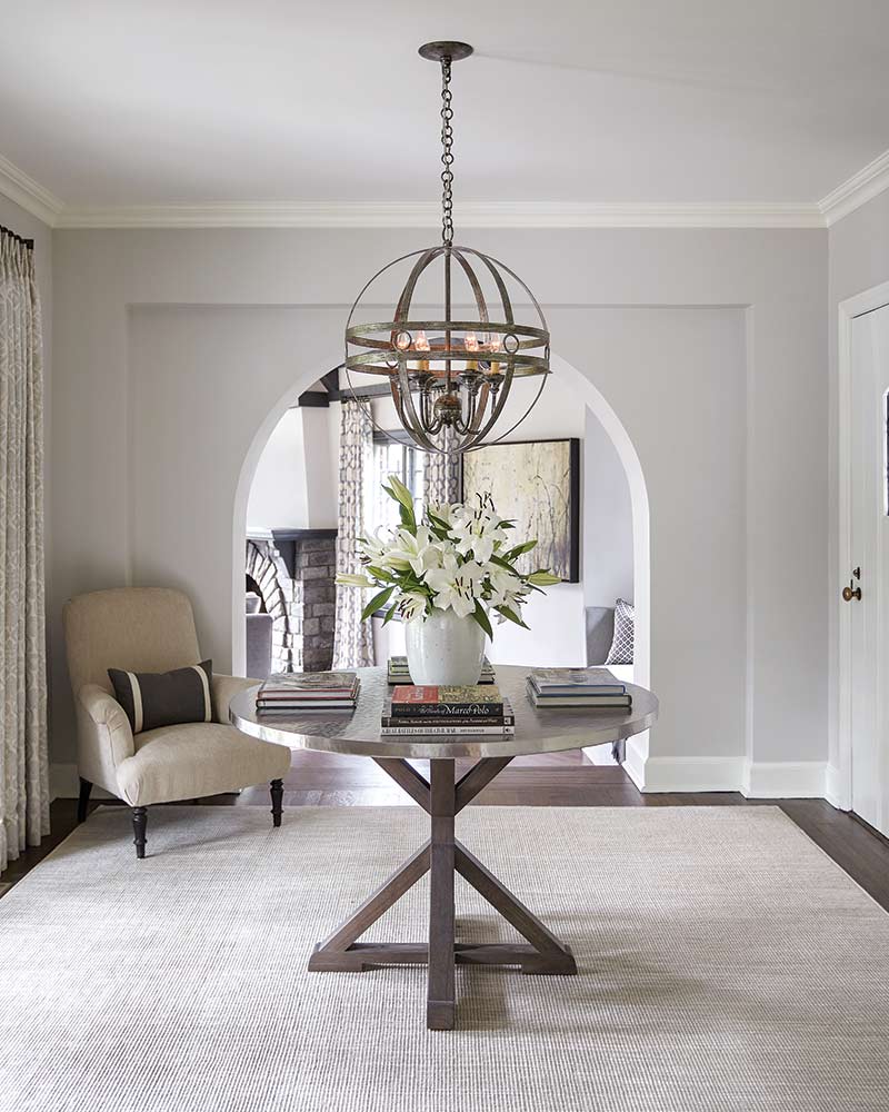 A foyer with a round table and floral arrangement under a modern light fixture.
