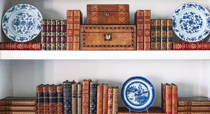 A book shelf with antique books, boxes, and Blue Willow china.