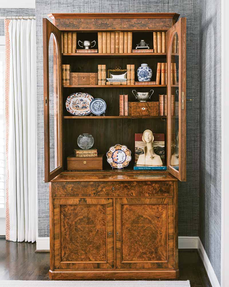 An antique cabinet filled with porcelain plates, leather books, and wooden boxes.