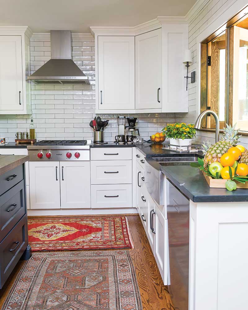 A white kitchen with hardwood floors and antique rugs.