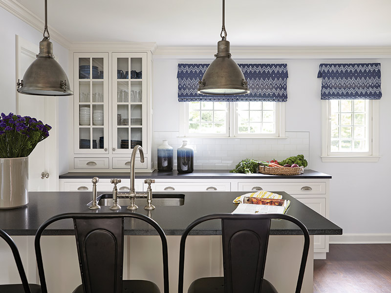 A white kitchen with black countertops and a blue-and-white roman shade.