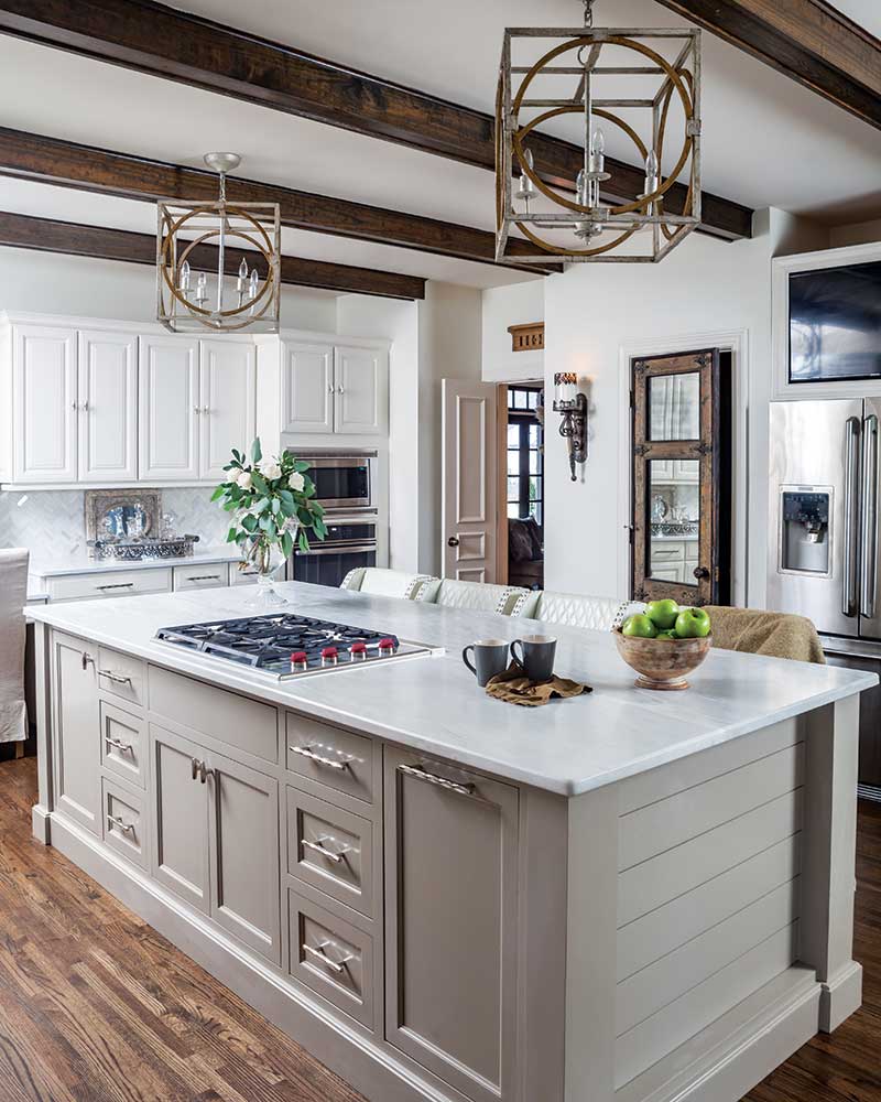 A kitchen with wooden beams, an island painted creme with a white marble countertop. 