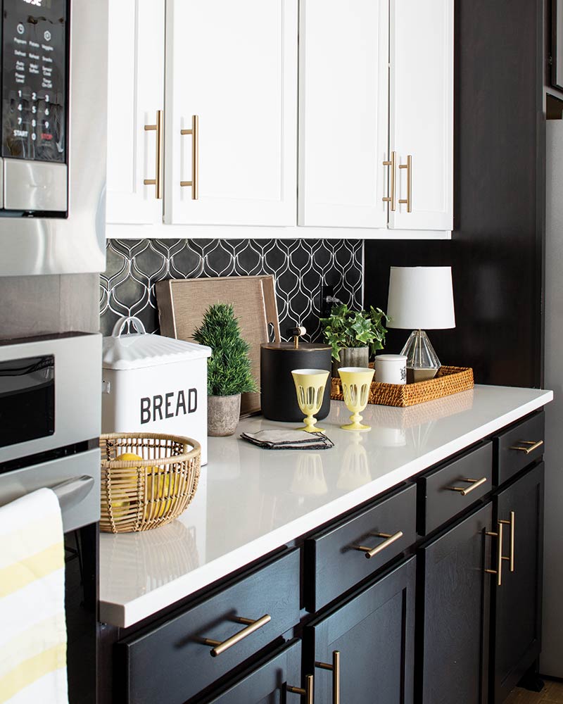 A kitchen with black lower cabinets, white countertops, and white upper cabinets.