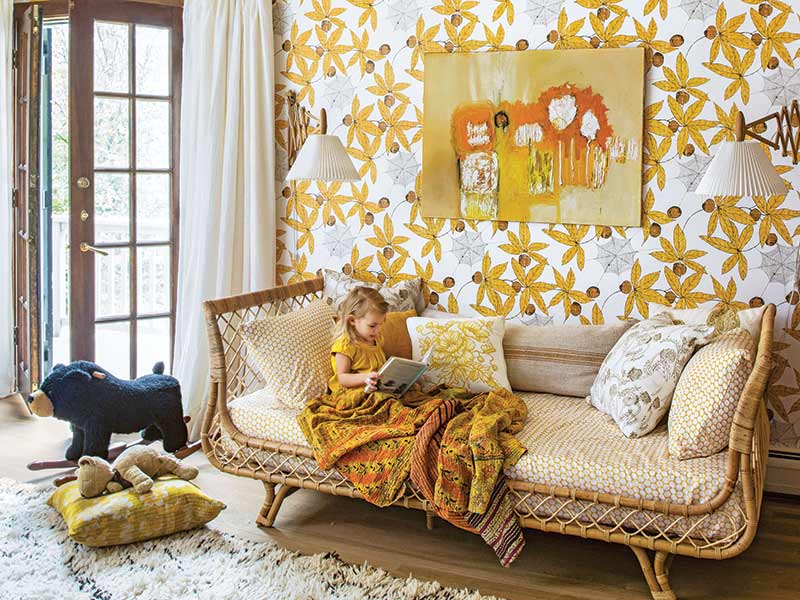 A bedroom with yellow floral wallpaper and a rattan daybed.