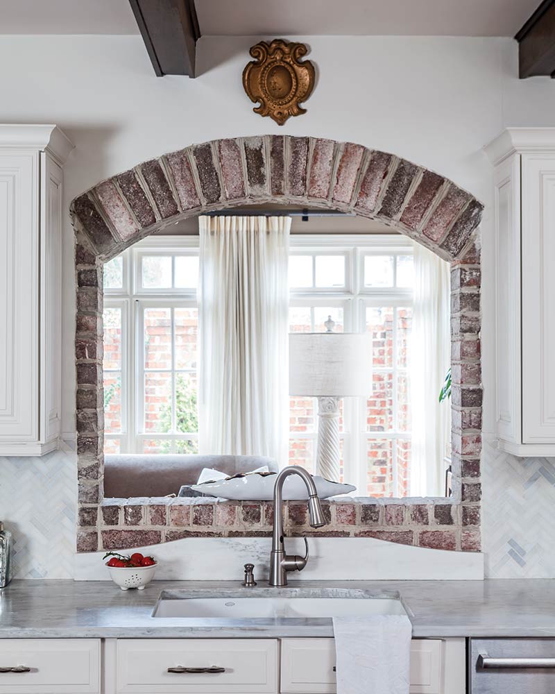 A sink with a brick-lined arched opening that leads to the sunroom.