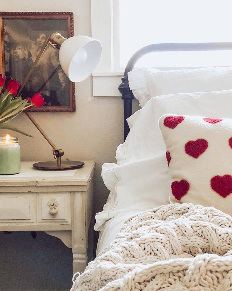 A bedroom with a white pillow with red hearts.