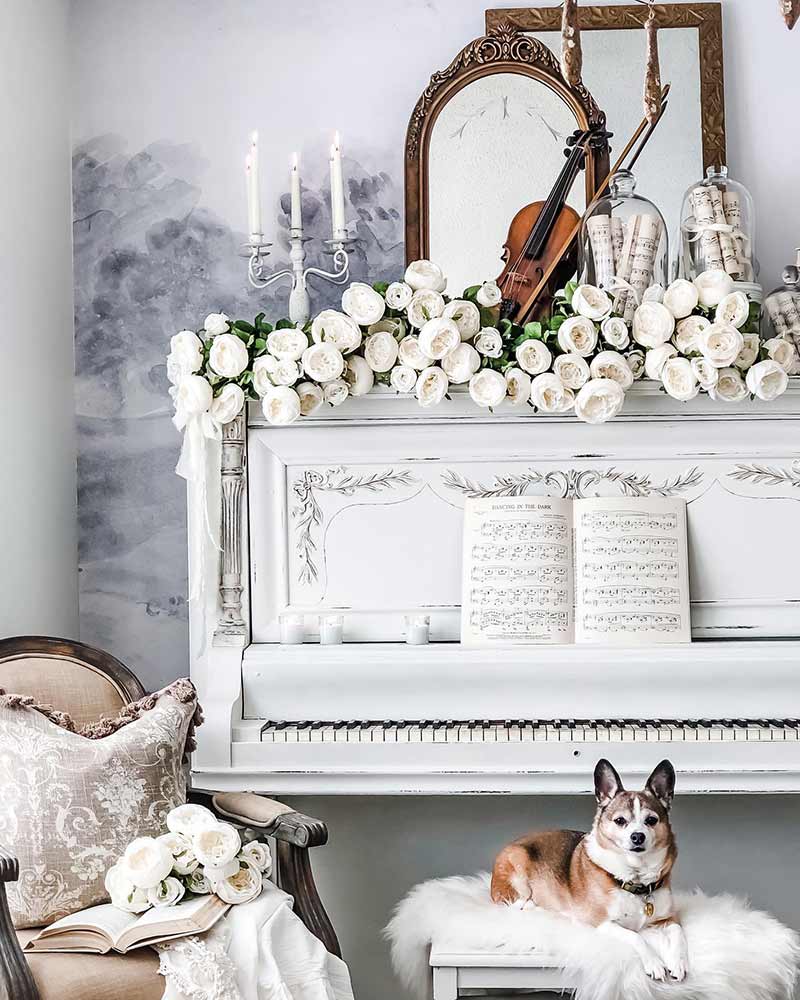 A white piano decorated with white roses and a violin.