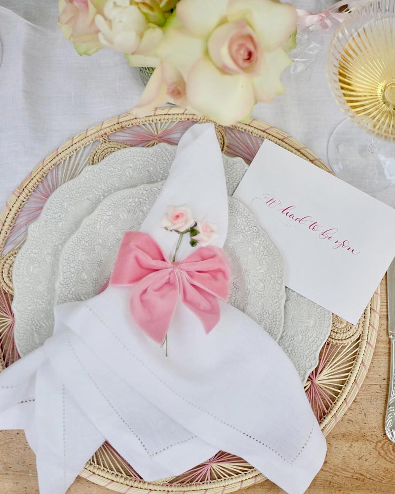 A white linen encircled with a pink velvet bow with a miniature blossom nestled inside.