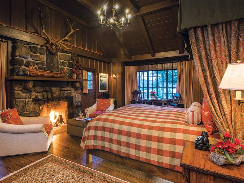 A bedroom with vaulted ceilings, a stone fireplace, and plaid furnishings.