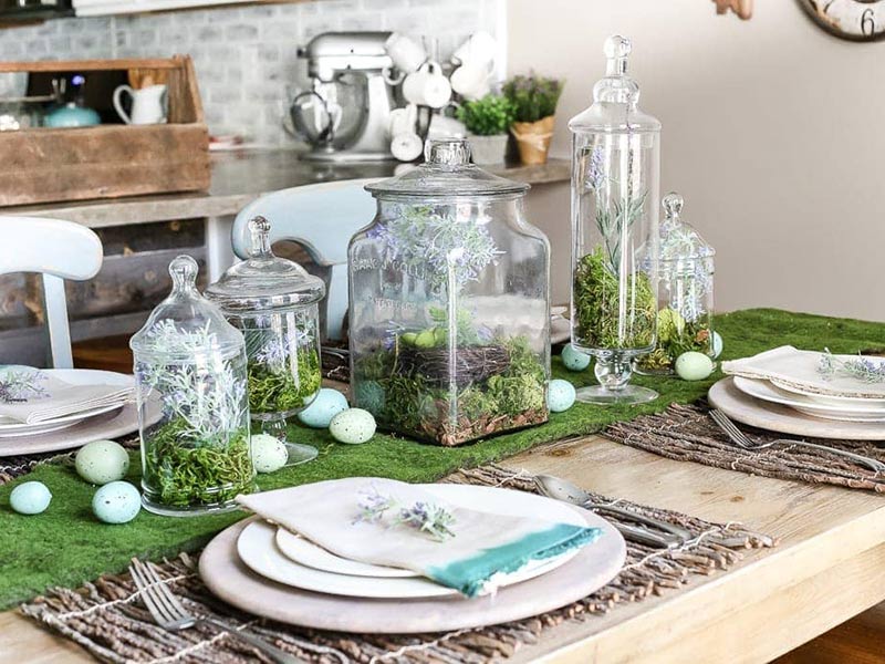 A tablescape with glass canisters filled with plants and Easter eggs.