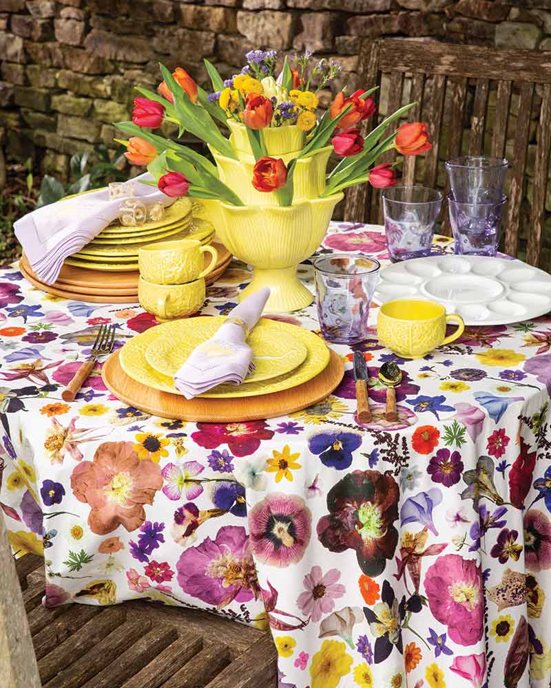 A tablescape with a floral tablecloth and a yellow tulipiere.