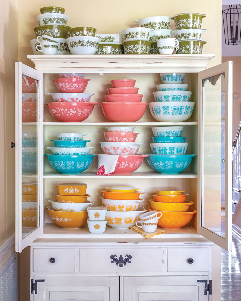 A white cupboard with multicolored pyrex dishes.