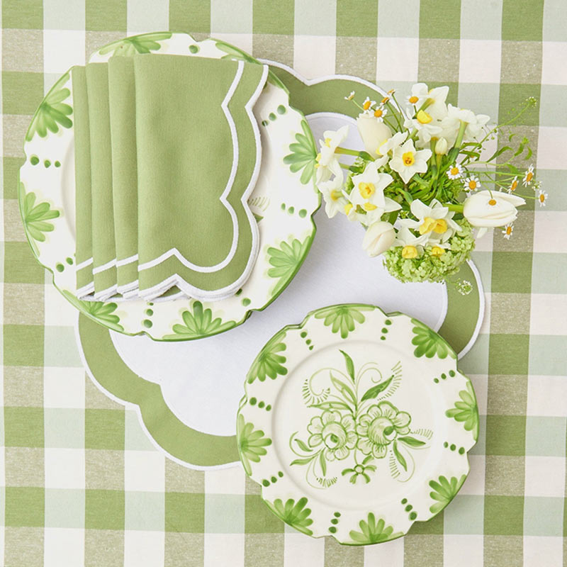 A green-and-white place setting with floral dishware atop a gingham tablecloth.