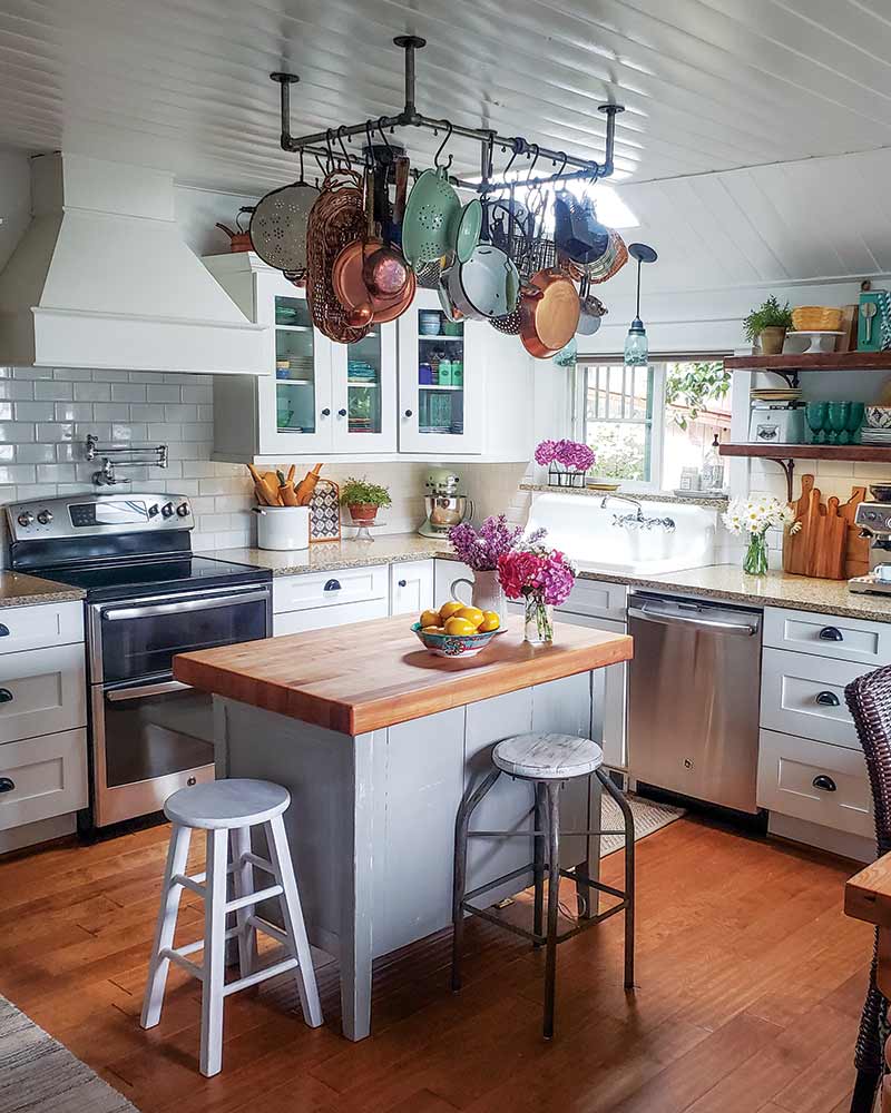 A white kitchen with a small island and a hanging pot rack.