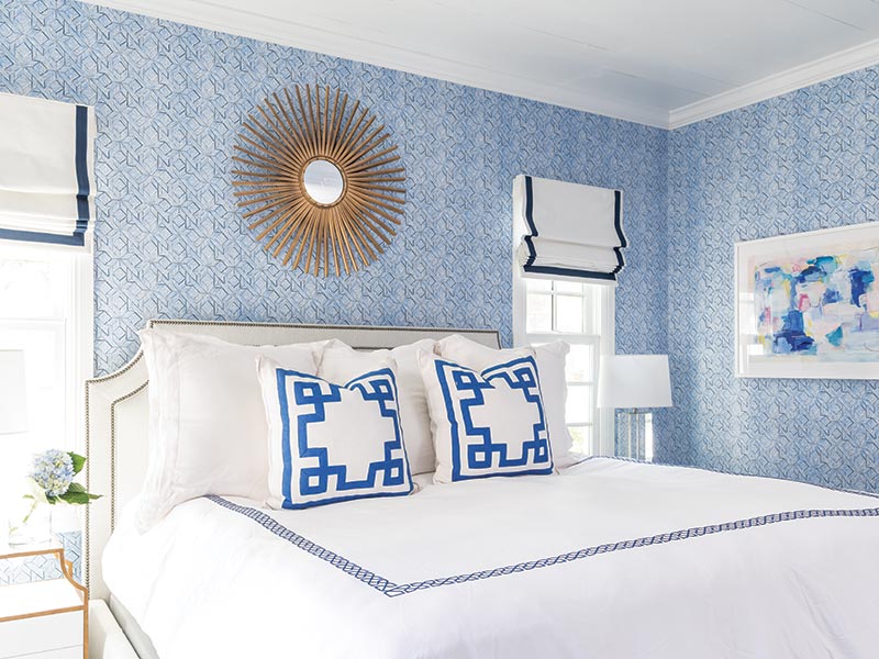 A bedroom with blue-and-white wallpaper and a sunburst mirror.