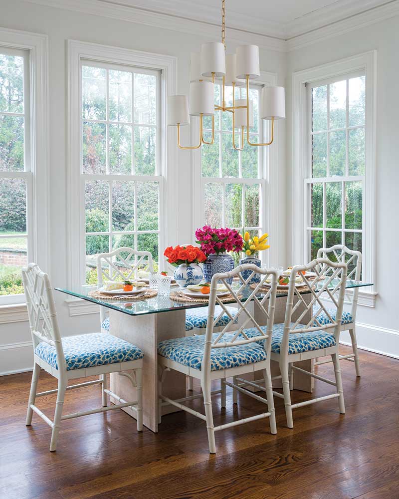 A breakfast nook with windows and white bamboo-style chairs.