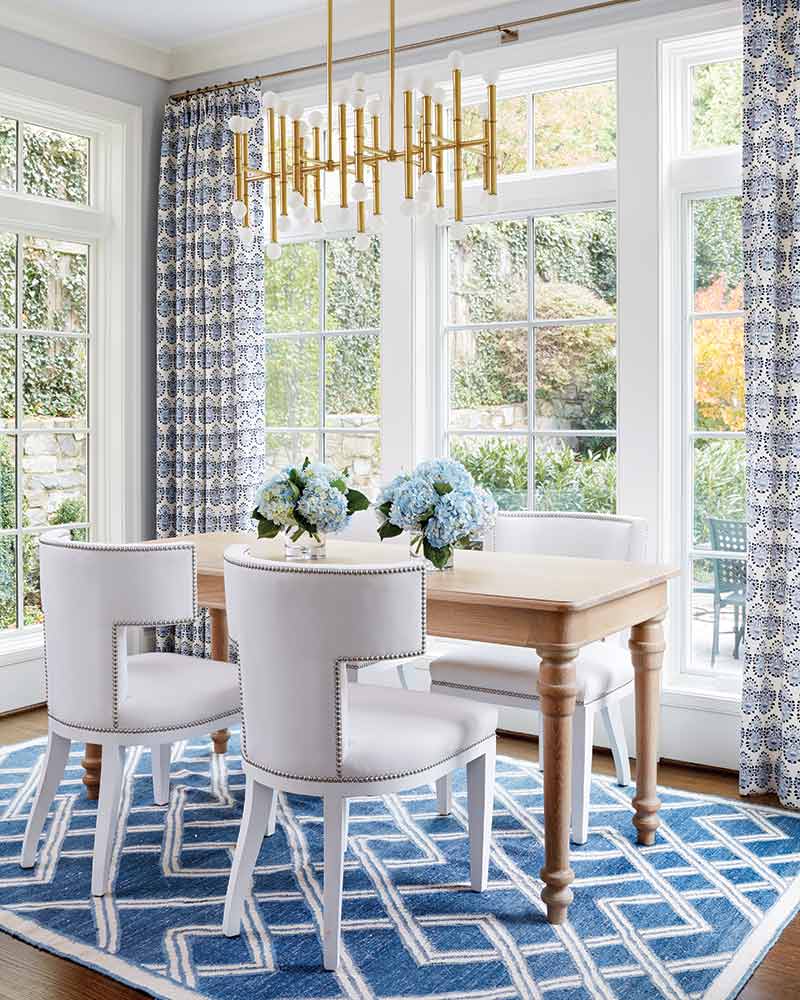 A breakfast nook with white chairs, a blue-and-white rug, and contemporary light fixture.