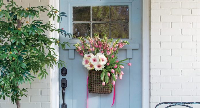 A sky blue front door with a hanging basket of pink flowers.