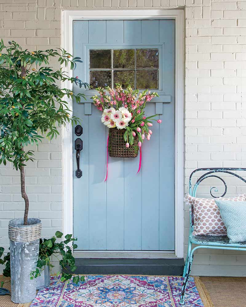 A sky blue door with a hanging basket of pink flowers.