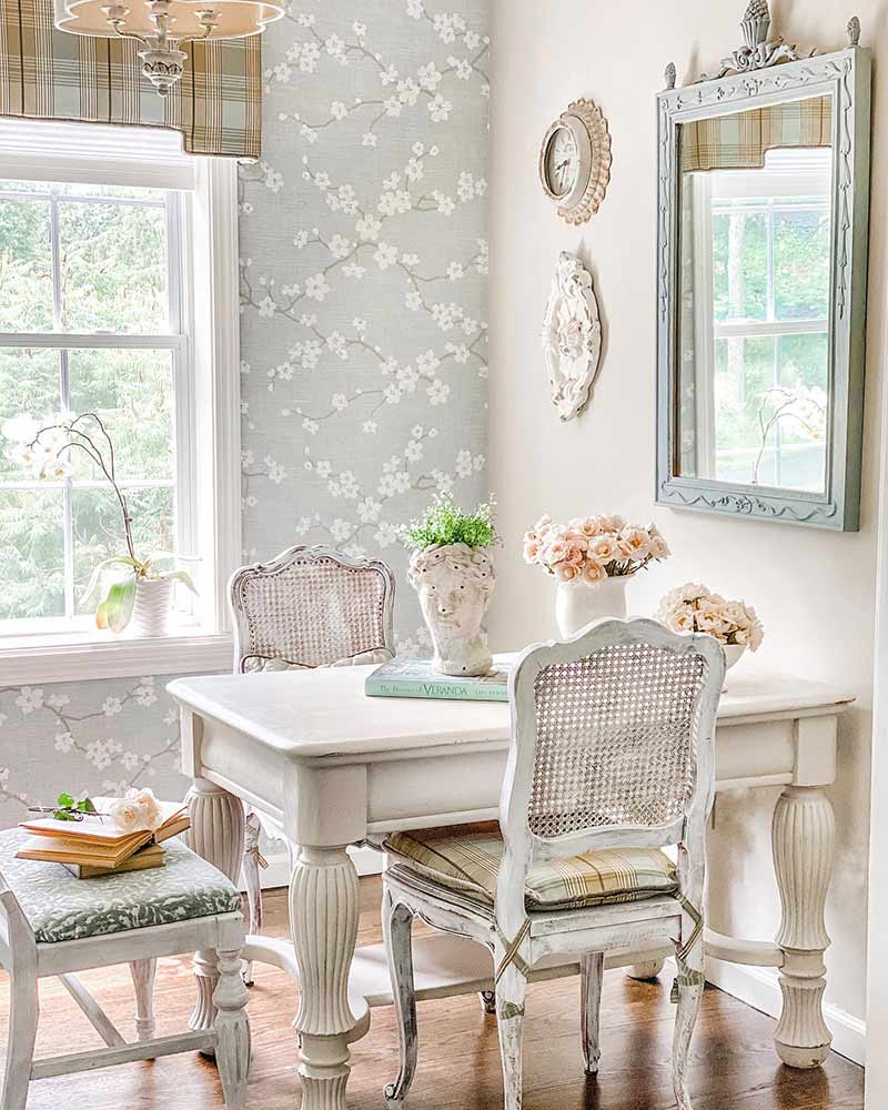 A breakfast nook with whitewashed furniture and cherry blossom-themed wallpaper.