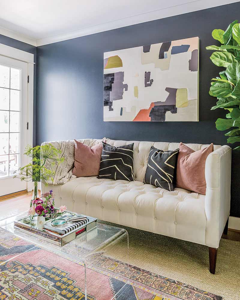 A den with navy walls and a white sofa and abstract artwork.